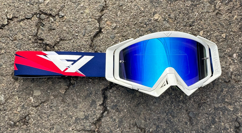 White goggles with blue lenses and a red, white and blue strap on a textured surface