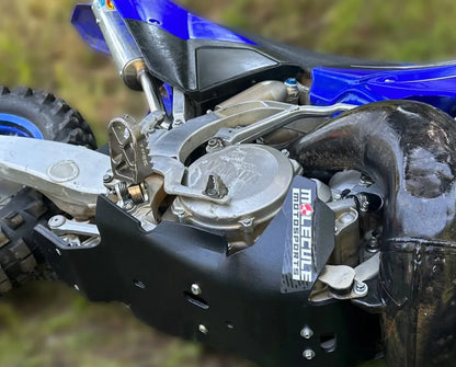 Close-up of a motorcycle engine with a Molecule Motorsports brand skid plate and logo on a blurred natural background