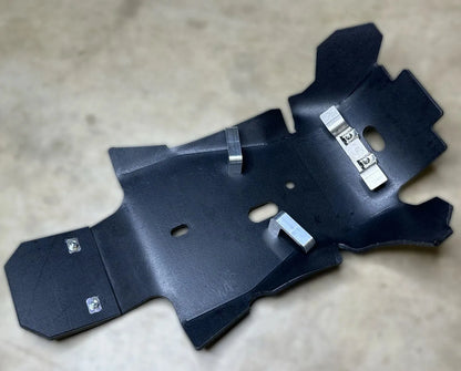 Black UHMW plastic dirt bike skid plate and metal bracket on a beige surface
