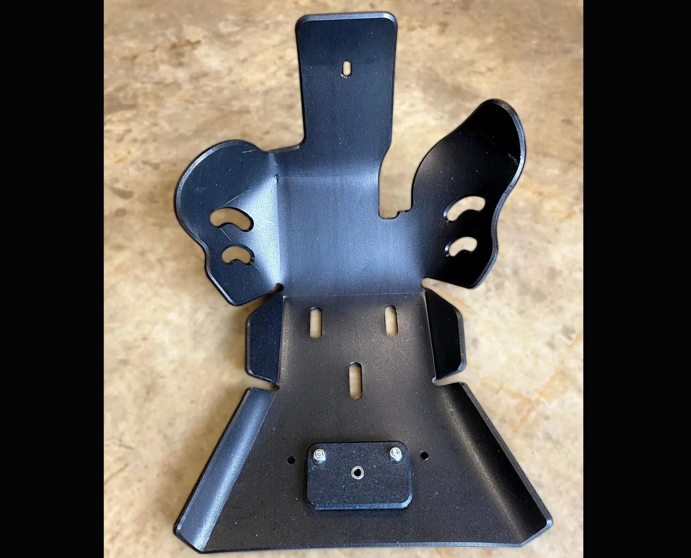 Black UHMW Skid Plate by Molecule Motorsports with a metal bracket on a beige surface