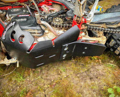 Close-up of a motorcycle chain and sprocket with a black protective skid plate cover on a grassy background.