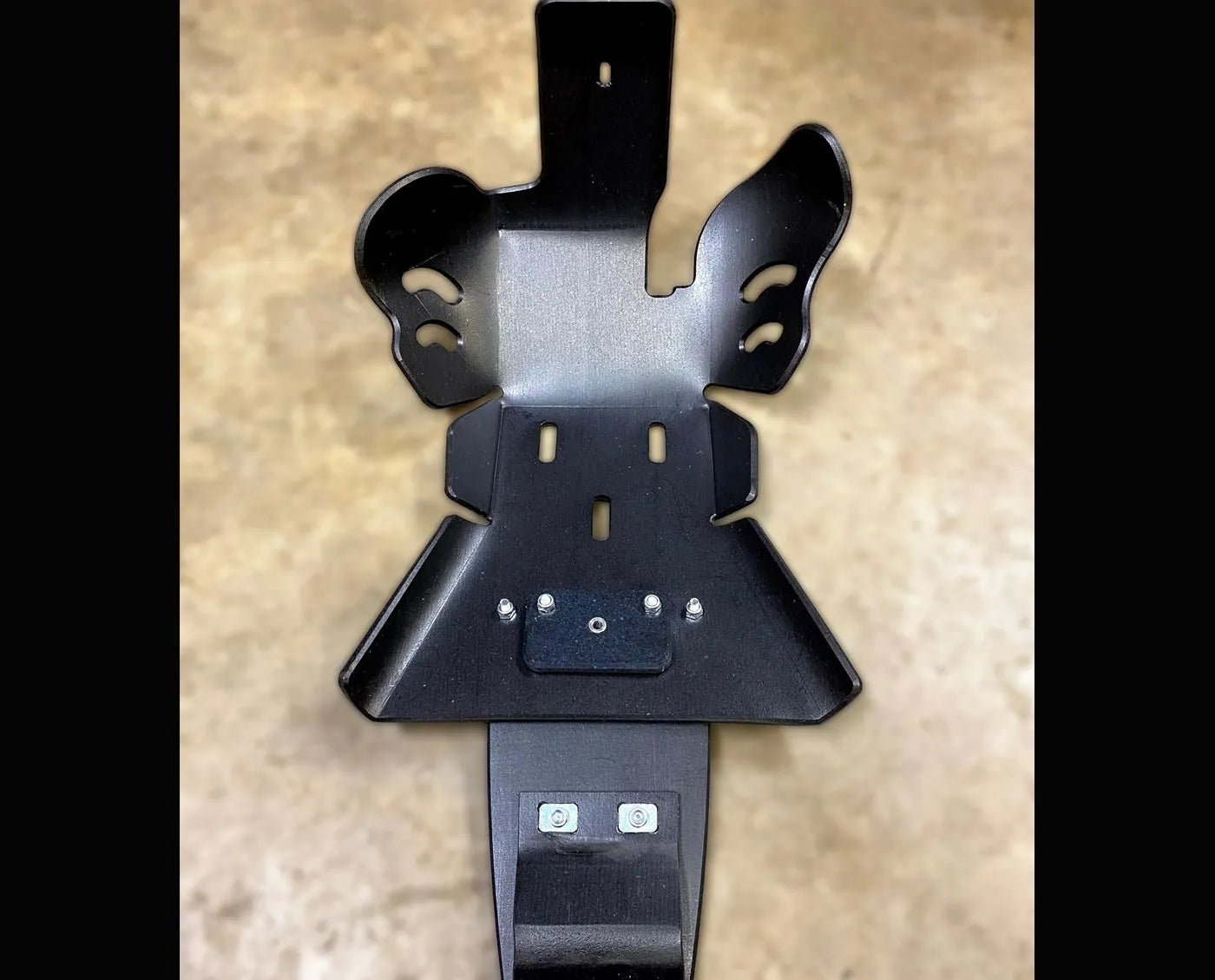 Black motorcycle skid plate by Molecule Motorsports on a beige surface