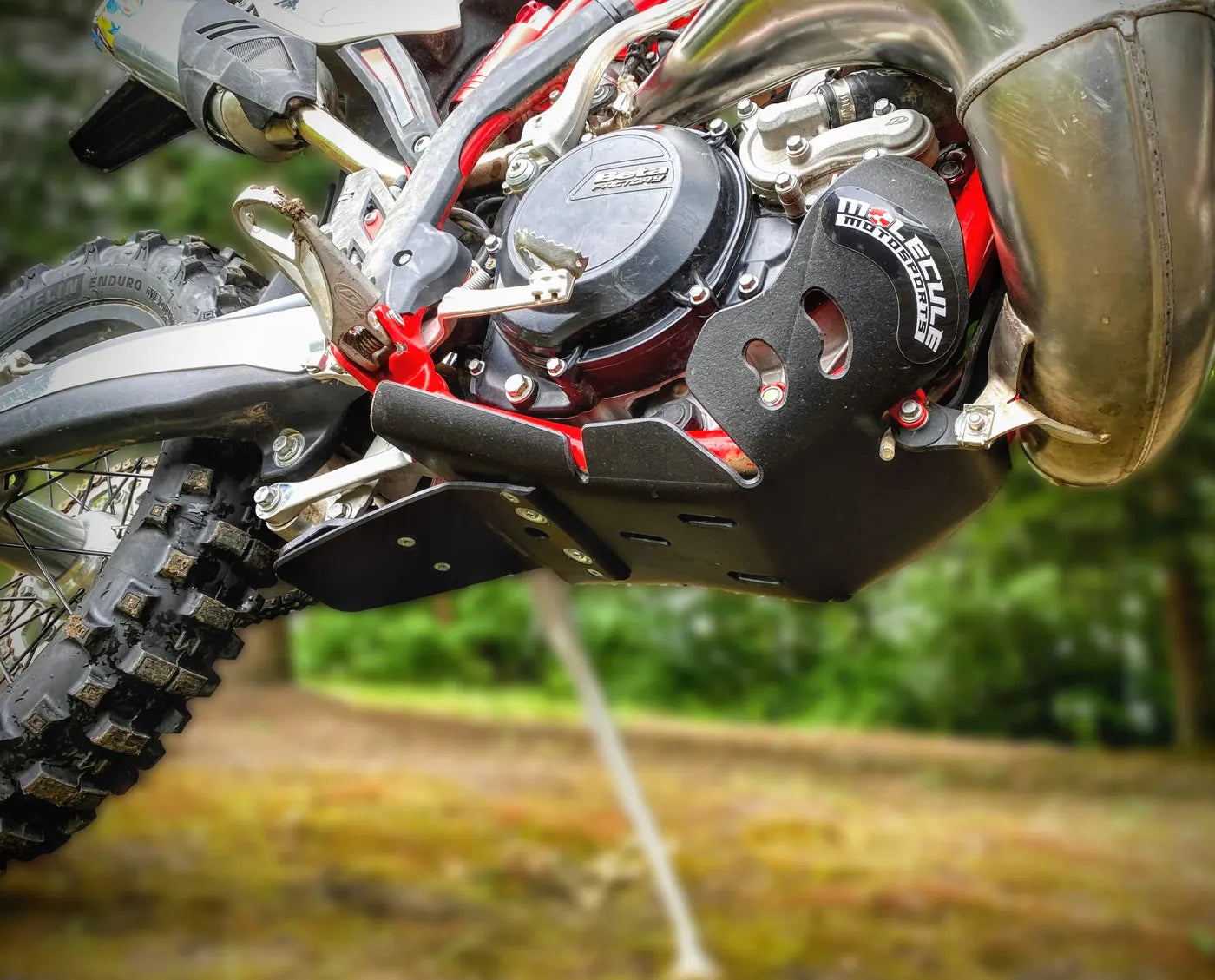 Close-up of a dirt bike with a focus on the skid plate, suspension and branding.