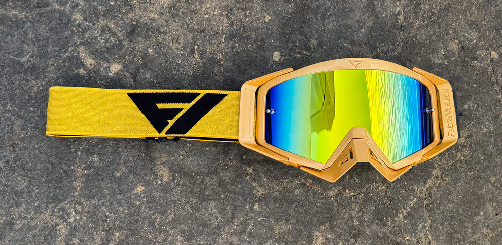 Pair of goggles with colorful lenses and a gold strap on a textured surface