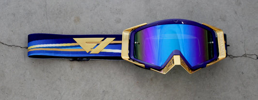 Gold and blue goggles with a reflective lens on a gray concrete surface