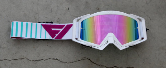 White goggles with a colorful lens and striped strap on a concrete surface