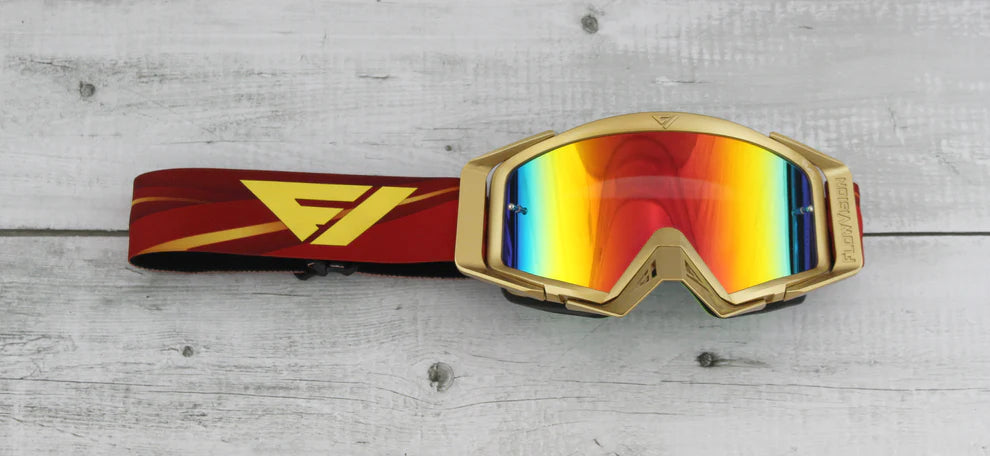 Gold goggles with a colorful lens and red and yellow strap on a wooden surface
