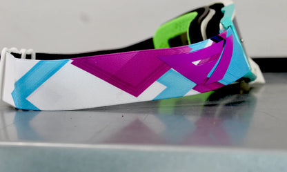 Colorful geometric-patterned goggle strap on a reflective surface with a blurred background