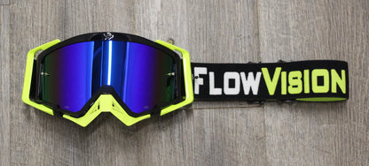 Moto goggles with blue reflective lenses and a black strap labeled 'FlowVision' on a wooden surface.
