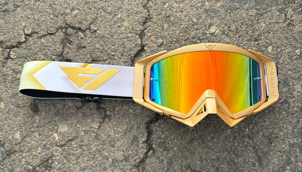 Gold-framed goggles with colorful lenses on a concrete surface