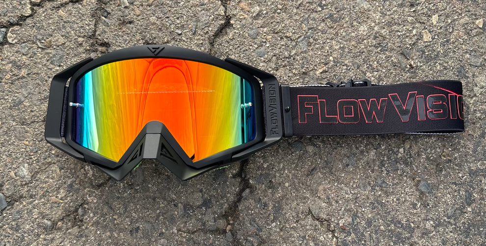 Goggles with colorful lens and 'FlowVision' strap on a concrete surface