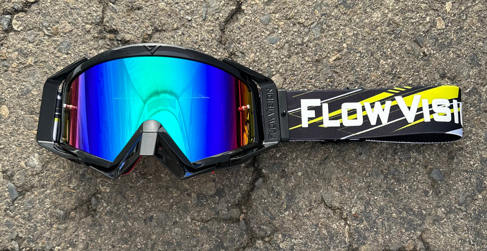 Goggles with reflective blue lens and 'Flow Vision' strap on a textured surface