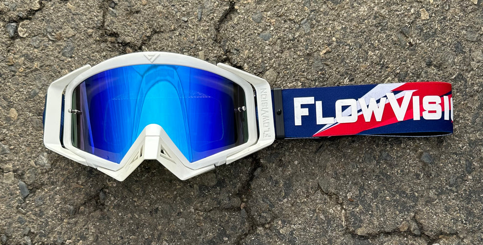 White goggles with blue lenses and a FlowVision strap on a textured surface