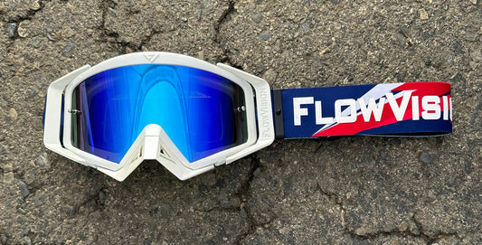 White goggles with blue lenses and a FlowVision strap on a textured surface