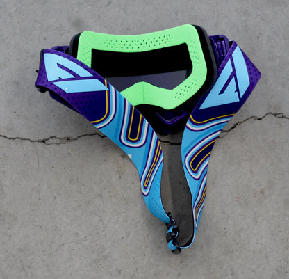 Colorful goggles with a purple, blue, and green design on a concrete surface