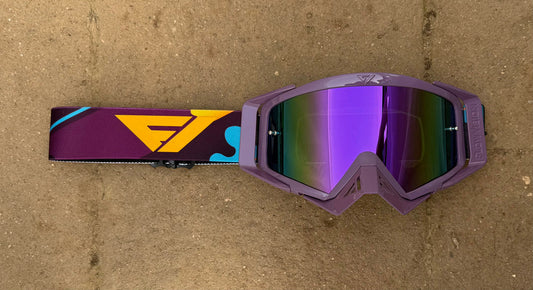 Purple goggles with a colorful strap on a brown surface