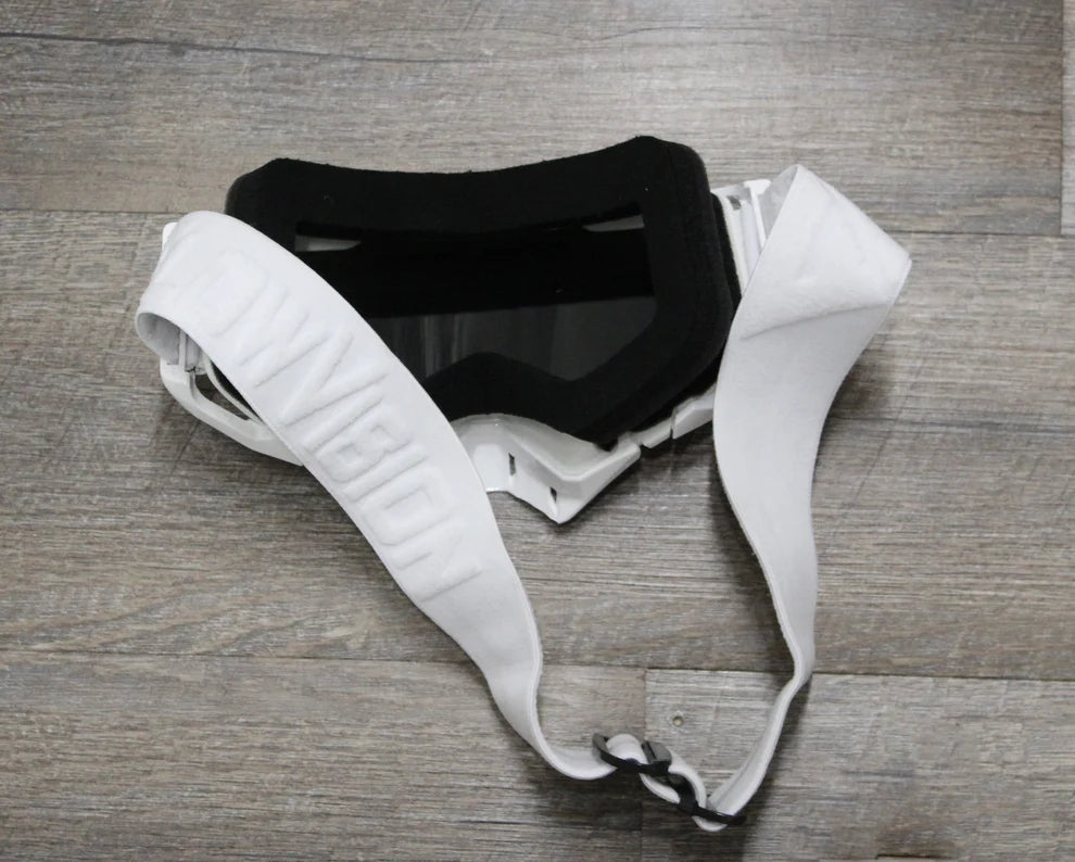 White goggles with black face foam and a white strap on a wooden surface