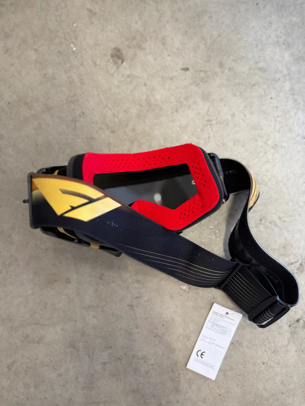 Red, yellow, and black motocross goggles on a gray concrete surface