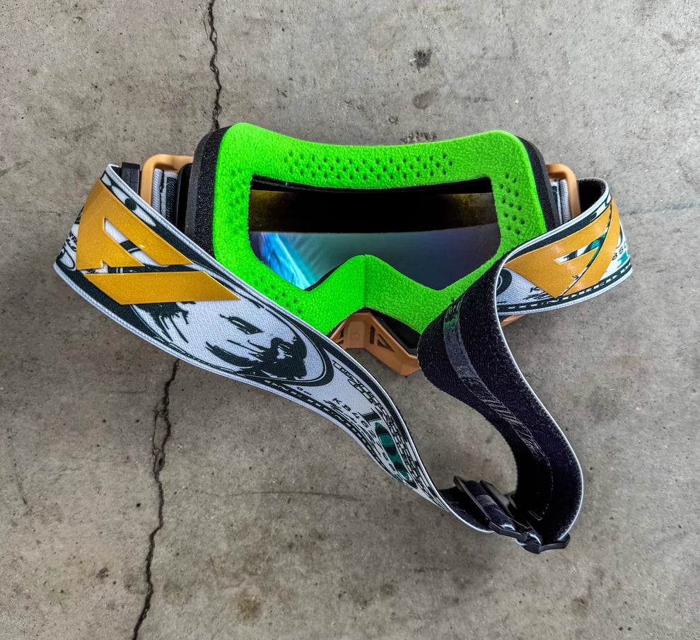 Green goggles with a colorful strap on a concrete surface