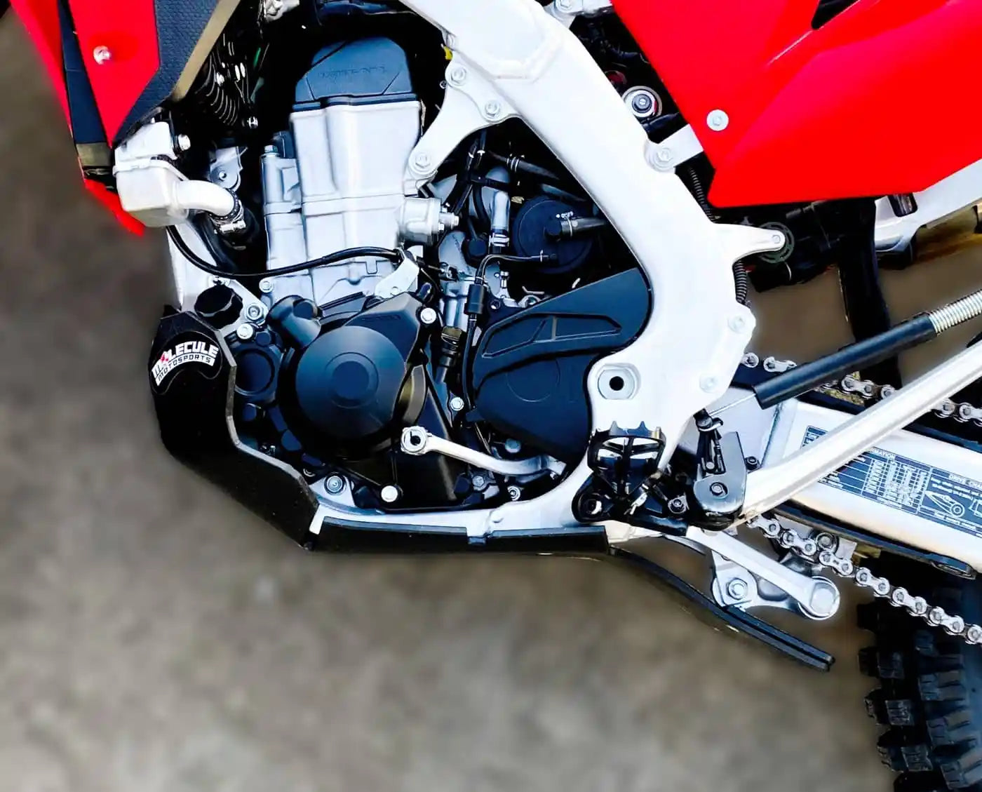 Close-up of a motorcycle engine, chain and skid plate on a blurred background