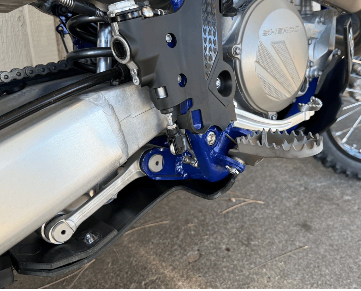 Close-up of a motorcycle's chain and sprocket area with a visible brand logo and skid plate.