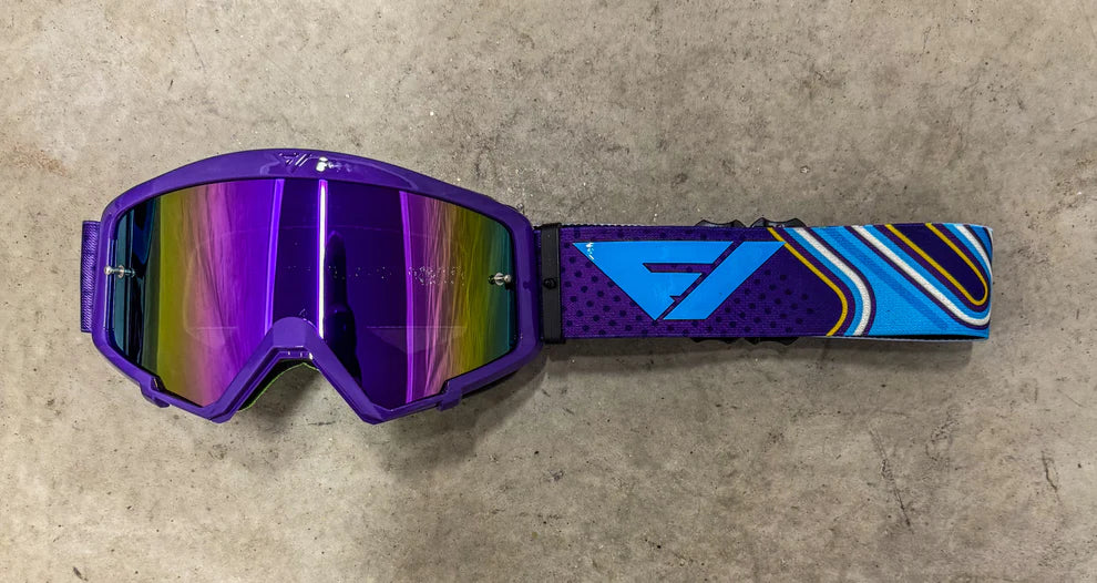 Purple goggles with a blue and yellow strap on a concrete surface
