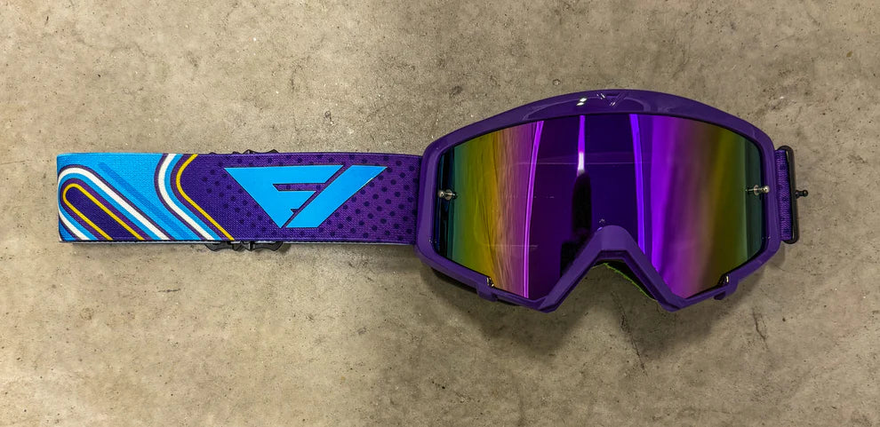Purple goggles with a colorful strap on a beige surface